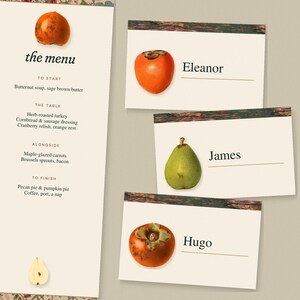 May include: A vertical menu card titled the menu with a list of food items and three rectangular place cards featuring illustrations of a persimmon or pear, with the names Eleanor, James, and Hugo printed next to the fruit illustrations.