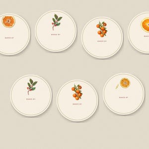 May include: Seven circular cream-colored labels with a thin border. Each label features a small botanical illustration of oranges, orange slices, or holly berries and leaves, with the text "BAKED BY" printed in small brown capital letters.