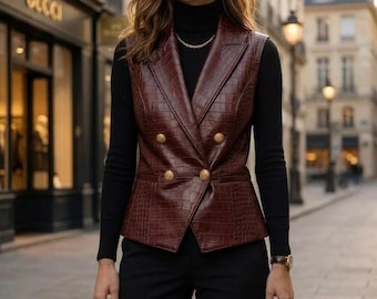 May include: A sleeveless, double-breasted vest in a deep burgundy faux leather with a crocodile-embossed texture. The vest features wide lapels, four gold-toned buttons arranged in two rows, and a tailored fit, worn over a black turtleneck.