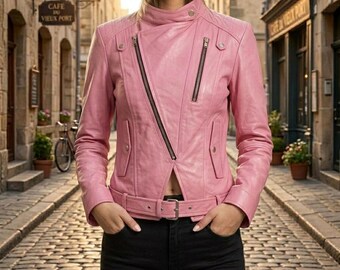 May include: A pink leather jacket featuring an asymmetrical front zipper closure, a high collar with a snap button, two vertical zippered chest pockets, and a matching waist belt with a silver-toned buckle, worn over black pants.
