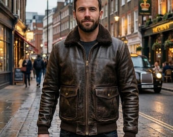 May include: A dark brown leather bomber jacket featuring a dark brown shearling collar, a full-length front zipper, two large front flap pockets with snap closures, and ribbed cuffs and hem, worn over a dark gray sweater and dark blue jeans.