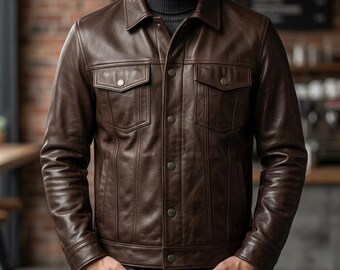 May include: A dark brown leather jacket featuring a classic collar, a button-front closure, and two chest pockets with buttoned flaps. The jacket is worn over a dark grey turtleneck sweater and paired with dark blue denim jeans.