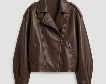 May include: A dark brown leather jacket featuring a wide notched collar, an asymmetrical front zipper closure, and two zippered side pockets. The long sleeves have zippered cuffs, and the shoulders are accented with epaulet details.