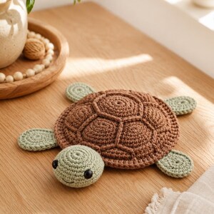 Könnte beinhalten: Ein gehäkeltes Schildkrötenspielzeug mit einem braunen Panzer in segmentierter Struktur sowie einem hellgrünen Kopf und Flossen. Die Schildkröte hat zwei kleine schwarze Perlenaugen und einen einfachen gestickten Mund aus Garn.