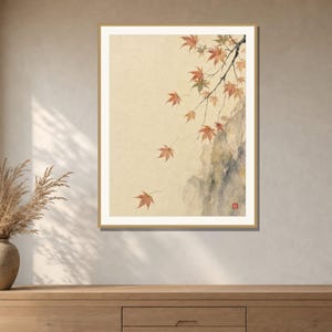 May include: A framed wall art print featuring a watercolor painting of delicate maple branches with orange and red leaves falling against a light beige background, with a dark gray rock formation on the right and a small red square seal mark.