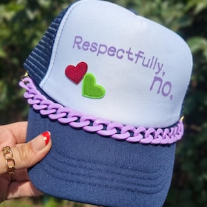 May include: A navy blue trucker hat with a white front panel featuring the purple text Respectfully, no. and two small embroidered hearts in red and green. A thick, light purple plastic chain is attached across the base of the front panel.