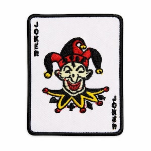 May include: A rectangular embroidered patch featuring a white background with a black border. The design depicts a jester face in red, black, and yellow, with the word JOKER written vertically in black text along the left and right sides.