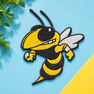 May include: An embroidered patch featuring a cartoon hornet with a yellow and black striped body, large black eyes, and white wings. The design is outlined in thick black thread, showcasing a stylised insect character with a determined expression.