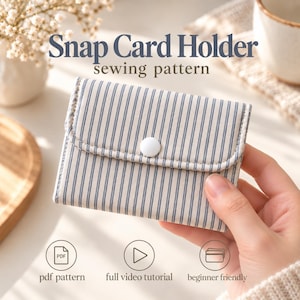 Puede incluir: Un tarjetero rectangular con un patrón de rayas verticales azules y beige, con un cierre de botón a presión blanco. El texto dice Snap Card Holder sewing pattern, pdf pattern, full video tutorial y beginner friendly.