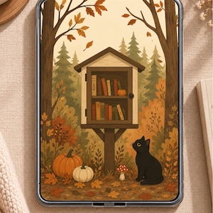 Op de afbeelding: Een digitale tablet met een illustratie van een kleine houten bibliotheekkast gevuld met boeken, geplaatst in een bos met herfstbladeren. Een zwarte kat zit op de grond bij twee pompoenen en een paddenstoel, omringd door gevallen bladeren.