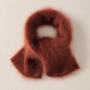 May include: A rust-colored scarf with a fuzzy, brushed texture. The scarf is arranged in a circular loop shape, showcasing the soft, long-fiber knit construction and the deep, warm reddish-brown hue of the material throughout the entire piece.
