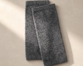 May include: A pair of dark gray arm warmers crafted from a soft, textured knit fabric. These rectangular accessories feature a simple, seamless design with a consistent heathered appearance throughout the material, providing full coverage.