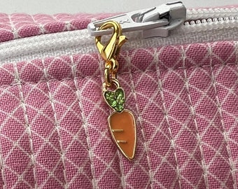 May include: A pink quilted zippered pouch with a white zipper and a gold carrot charm.