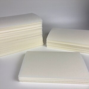 May include: Three stacks of white cleaning cloths, each stack is a different size. The stacks are on a white surface.