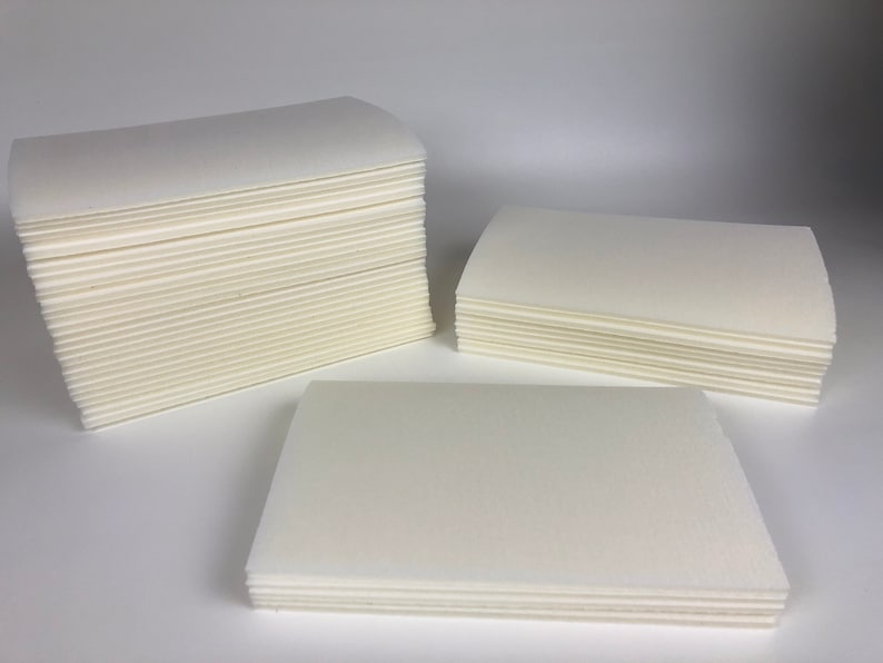 May include: Three stacks of white cleaning cloths, each stack is a different size. The stacks are on a white surface.