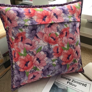 Puede incluir: Una almohada floral con un estampado floral morado y rosa. La almohada tiene una cremallera y est&aacute; hecha con un patr&oacute;n de almohada con cremallera simple. El texto en el patr&oacute;n dice "Simple Zippered Pillow. Instructions for adding professional looking zippered backs to all your pillow projects."