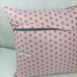 Puede incluir: Una almohada rosa con un patr&oacute;n floral blanco y marr&oacute;n. La almohada tiene una cremallera.