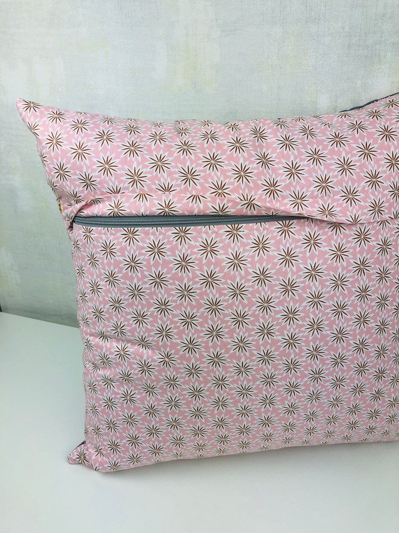 Puede incluir: Una almohada rosa con un patr&oacute;n floral blanco y marr&oacute;n. La almohada tiene una cremallera.