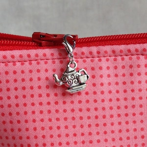 May include: A red zippered pouch with a white polka dot pattern. A silver teapot charm is attached to the zipper pull.