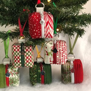 May include: Six small zippered pouches with Christmas-themed fabric designs. The pouches are hanging from a Christmas tree and are decorated with red, green, and white fabric. The pouches are about 4 inches tall and 3 inches wide.
