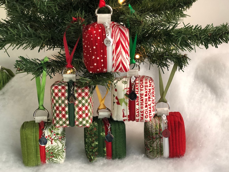 May include: Six small zippered pouches with Christmas-themed fabric designs. The pouches are hanging from a Christmas tree and are decorated with red, green, and white fabric. The pouches are about 4 inches tall and 3 inches wide.