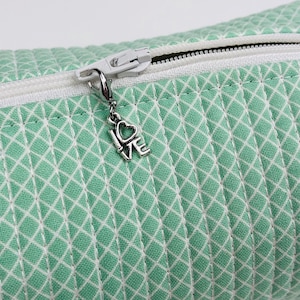 May include: A green zippered pouch with a white diamond pattern and a silver charm that says "I Love You".