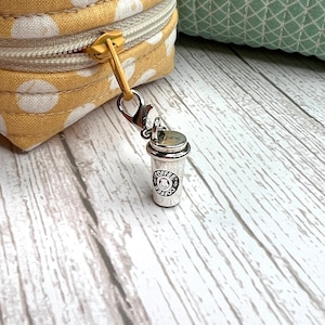May include: Silver charm in the shape of a coffee cup with the word "Coffee" on it. The charm is attached to a silver clip.