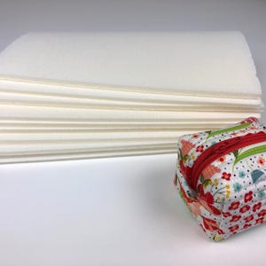 May include: A stack of white paper sheets with a small floral patterned zippered pouch in the foreground.