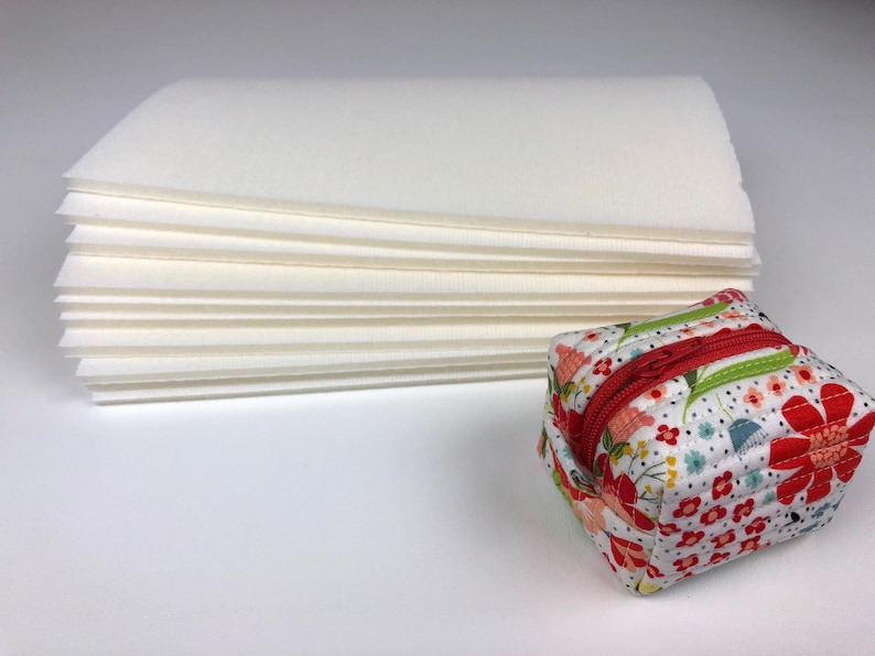 May include: A stack of white paper sheets with a small floral patterned zippered pouch in the foreground.