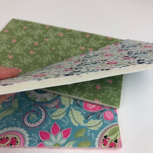 May include: Three pieces of fabric with floral patterns. The top piece is green with small white flowers, the middle piece is white with small blue and pink flowers, and the bottom piece is blue with pink and green flowers.