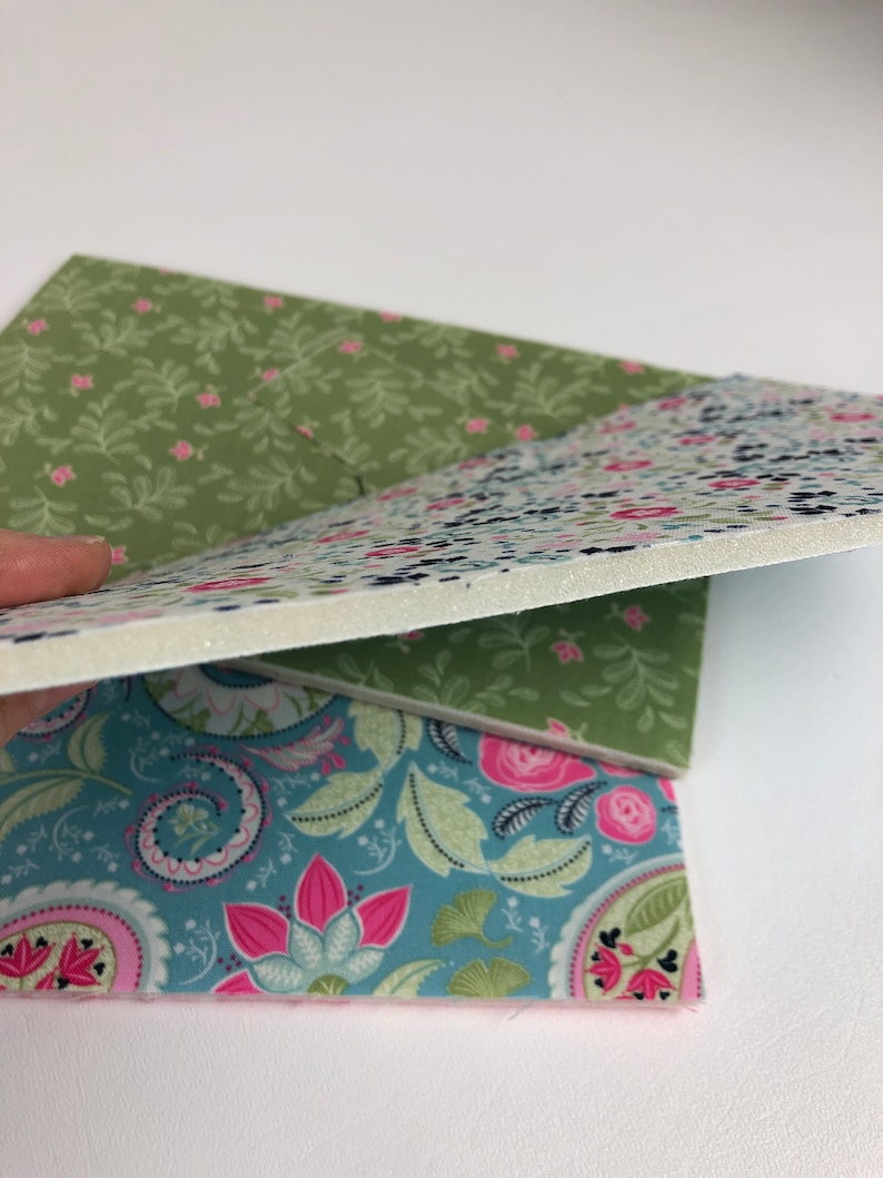 May include: Three pieces of fabric with floral patterns. The top piece is green with small white flowers, the middle piece is white with small blue and pink flowers, and the bottom piece is blue with pink and green flowers.