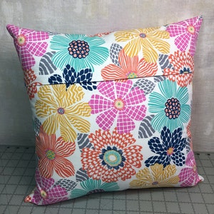 Puede incluir: Una almohada blanca con un patr&oacute;n floral en tonos de rosa, naranja, amarillo, azul y verde. La almohada tiene una cremallera en la parte posterior.