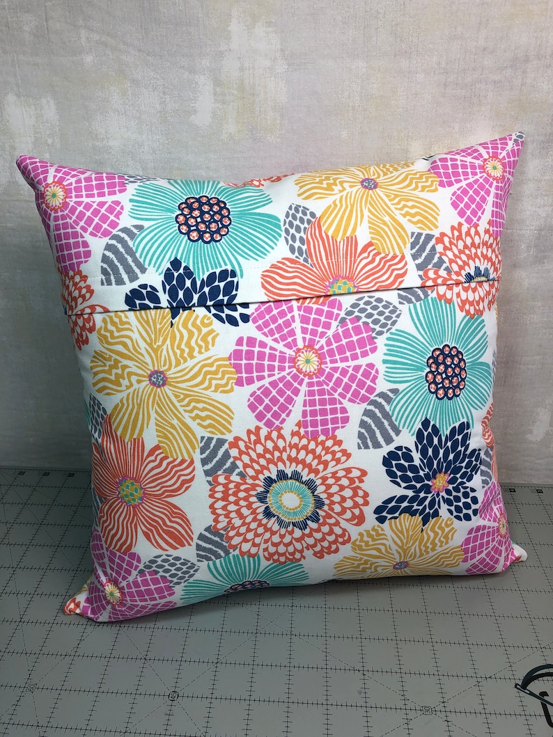 Puede incluir: Una almohada blanca con un patr&oacute;n floral en tonos de rosa, naranja, amarillo, azul y verde. La almohada tiene una cremallera en la parte posterior.