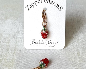 May include: Two gold zipper charms featuring a red and green strawberry design. The charms are attached to a gold zipper pull. The charms are labeled "Zipper charms" and "Bodobo Bags by Ticklegrass Designs".