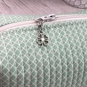 May include: A green zippered pouch with a white diamond pattern and a silver four-leaf clover zipper pull.