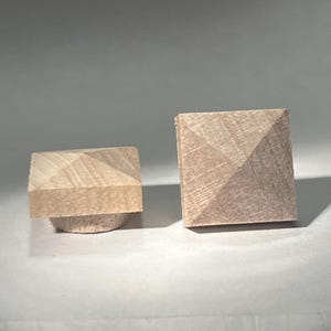 May include: Two wooden square pyramid shaped finials. The finials are light brown in color and have a smooth, slightly textured surface.
