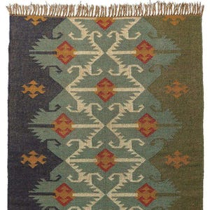 May include: A rectangular woven rug featuring a central vertical band of teal with geometric patterns in cream, red, and orange. The left side is dark charcoal and the right side is olive green, both with small orange motifs. The top edge has fringe.