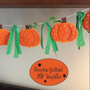 May include: A pumpkin garland featuring orange felt pumpkins with brown stems and gold sequins, accented by green polka-dot fabric ribbons and green pipe cleaner vines strung on a white cord. An orange oval label reads Pumpkin Garland PDF Template.