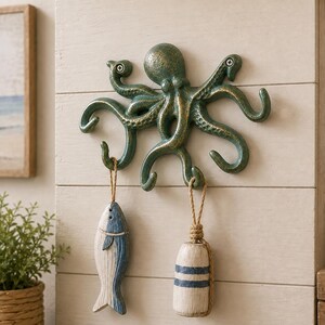 May include: A wall-mounted octopus hook rack in a dark green finish with gold highlights. The octopus has eight curved tentacles that serve as hooks. Two decorative items, a wooden fish and a cylindrical buoy, hang from the lower tentacles.