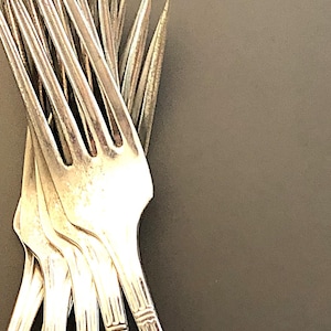 May include: A set of eight silver forks with ornate handles. The forks are arranged in a fan shape, with the tines pointing upwards.