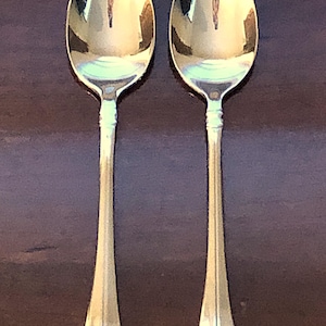 May include: Two silver spoons with ornate handles. The spoons are polished and reflect light.
