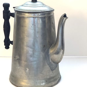 May include: A vintage silver aluminum coffee pot with a black wooden handle and lid knob. The pot has a classic design with a rounded body and a spout.
