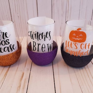 May include: Three wine glasses with glitter bottoms and Halloween-themed vinyl decals. The glasses say "More Boo's Please", "Witches Brew", and "Let's Get Smashed" with a pumpkin graphic.