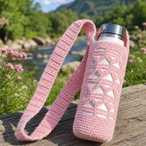 Può includere: Una borraccia in metallo bianco inserita in una custodia all'uncinetto rosa chiaro con un motivo geometrico traforato e una lunga tracolla all'uncinetto abbinata. La custodia presenta una base solida e un cinturino testurizzato e a coste.