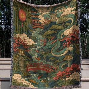 May include: A woven throw blanket featuring a detailed illustration of a green dragon winding through a landscape with red bridges, stone lanterns, a pagoda, bamboo, and koi fish swimming in a river. The edges have a decorative fringe finish.