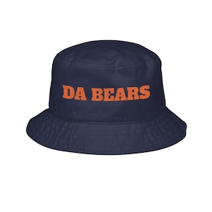 May include: A navy blue bucket hat featuring the text DA BEARS embroidered in orange across the front crown. The hat has a downward-sloping brim and a rounded top, constructed from a solid fabric with a consistent dark blue color throughout.