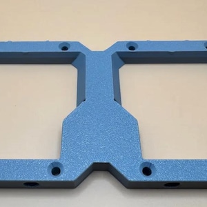 May include: A rectangular blue frame with a textured finish featuring two large square cutouts in the center. The frame has eight circular mounting holes positioned along the top and bottom edges, providing a structured and symmetrical design.