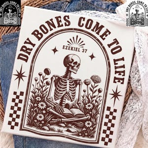 Könnte beinhalten: Ein weißer Leinwanddruck mit einer dunkelbraunen Illustration eines Skeletts, das in einem Blumenfeld sitzt und ein Buch liest. Der Text "DRY BONES COME TO LIFE" und "EZEKIEL 37" ist in einem Bogen über dem Skelett mit Schachbrettmustern gedruckt.