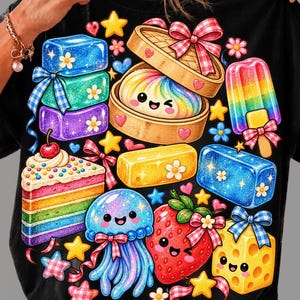 May include: A black t-shirt featuring a vibrant graphic print of various colorful items including a rainbow layer cake, a smiling jellyfish, a strawberry, a bamboo steamer with a rainbow bun, a rainbow popsicle, and several glittery blocks.