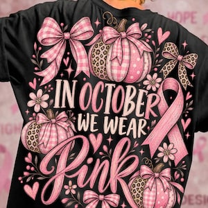 Op de afbeelding: Een zwart t-shirt met een grafische print van drie roze pompoenen versierd met luipaard- en ruitpatronen, roze strikken, kleine bloemen, hartjes en een roze bewustzijnslint. De tekst luidt, In October We Wear Pink.